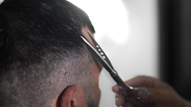Barbeiro tatuado faz corte de cabelo para o cliente na barbearia usando tesoura e pente, corte de cabelo homem e barbear no cabeleireiro, barbearia e salão de barbear — Vídeo de Stock