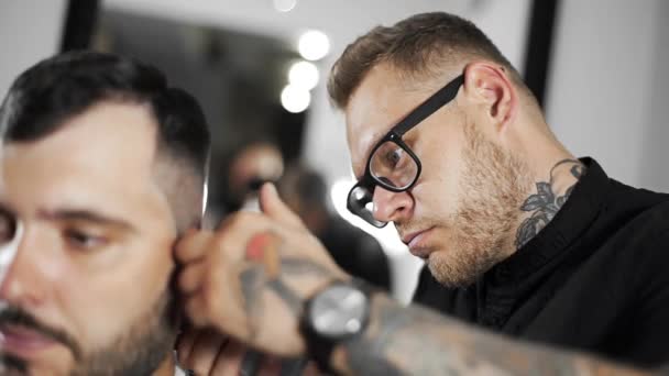 Fryzjer tattoed sprawia, że fryzura dla klienta o fryzjera za pomocą hairclipper, mans golenia o salon fryzjerski, fryzjer i salon golenie i strzyżenie — Wideo stockowe