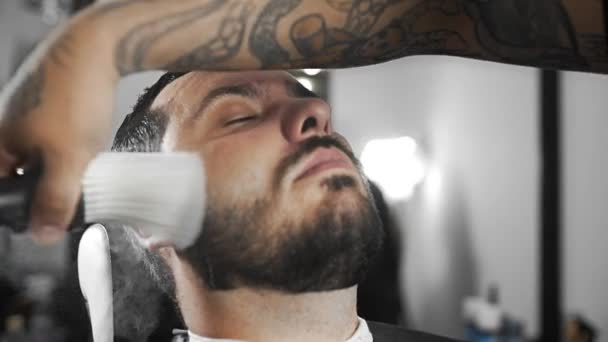 Barbeiro empurra cabelos cortados de clientes ombros por escova, barbeiro tatuado faz corte de cabelo para o cliente na barbearia, homem corte de cabelo e barbear no cabeleireiro, barbearia e barbear — Vídeo de Stock