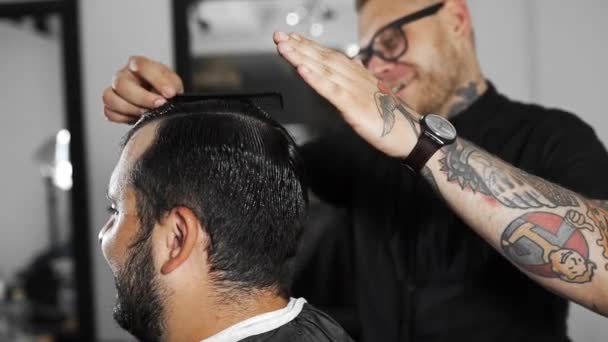 Barbier tatoué fait coiffure avec gel pour les cheveux pour le client après la coupe de cheveux au salon de coiffure, mans coupe de cheveux et le rasage au salon de coiffure, salon de coiffure et de rasage — Video