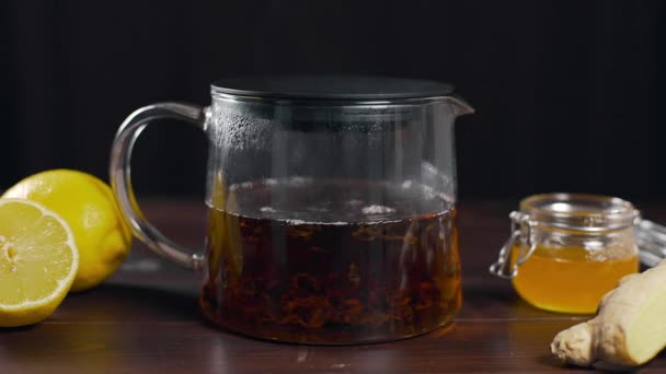 Гарячий чорний чай заварюють у скляному чайнику, вітамінний чай з лимоном, імбиром та медом, п'ють проти хвороби, гарячі напої — стокове відео