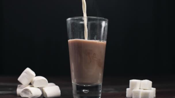 O leite é adicionado à bebida quente de cacau, fazendo o cacau quente com leite e marshmallows, vidro isolado de cacau. — Vídeo de Stock