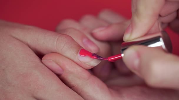 Маникюрша красит ногти клиентов с бежевым оттенком лака для ногтей на красном фоне, макияж и ногти, закрыть нанесение лака для ногтей — стоковое видео
