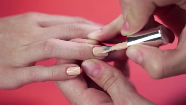 Manicurista dipinge le unghie dei clienti con smalto beige tinta sullo sfondo rosso, trucco e unghie, da vicino di applicare smalto — Video Stock