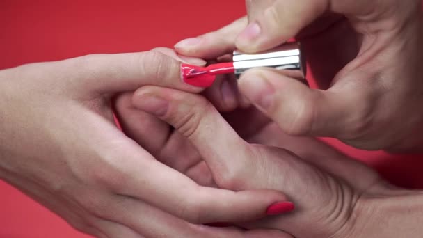 Manicura pinta las uñas de los clientes con esmalte de uñas de tinte beige en el fondo rojo, maquillaje y uñas, primer plano de la aplicación de esmalte de uñas — Vídeo de stock