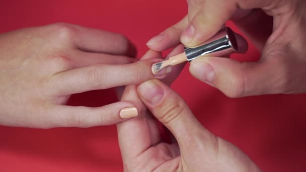 Manicura pinta las uñas de los clientes con esmalte de uñas de tinte beige en el fondo rojo, maquillaje y uñas, primer plano de la aplicación de esmalte de uñas — Vídeo de stock