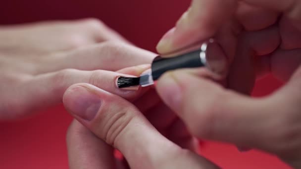 Manicura pinta las uñas de los clientes con esmalte de uñas de tinte beige en el fondo rojo, maquillaje y uñas, primer plano de la aplicación de esmalte de uñas — Vídeos de Stock