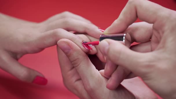 Manicura pinta las uñas de los clientes con esmalte de uñas de tinte beige en el fondo rojo, maquillaje y uñas, primer plano de la aplicación de esmalte de uñas — Vídeos de Stock