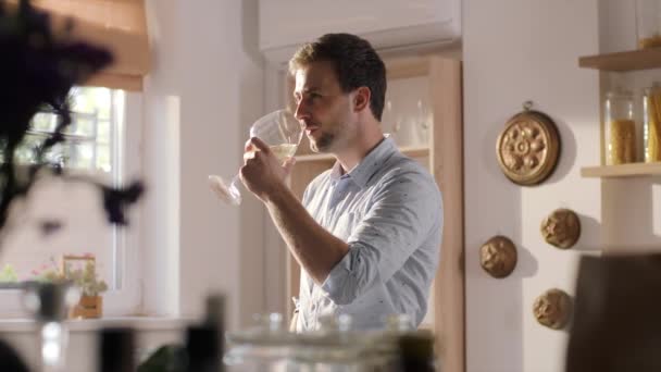 Young man drinks white wine from the big glass on the kitchen in the sunny summer day, tasting of wines, home party, wine after dinner — Stock Video