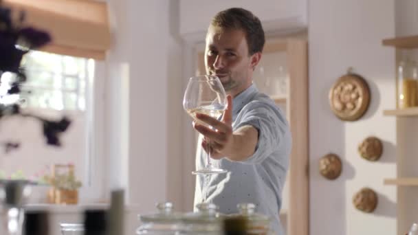 Mann prostet der Kamera mit einem Glas Weißwein zu, junger Mann trinkt Wein aus dem Glas, Weinverkostung, Heimatparty, Wein nach dem Abendessen, sonniger Sommertag, 4k uhd Zeitlupe — Stockvideo