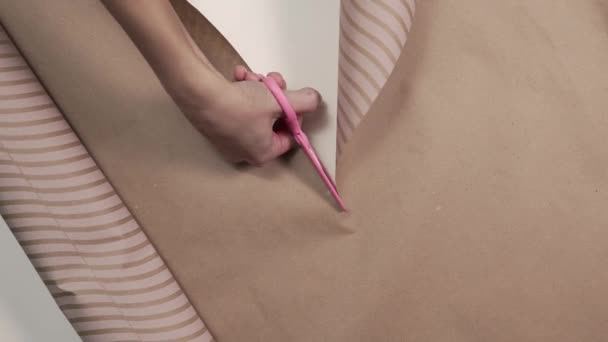 Gros plan du papier d'emballage coupé par des ciseaux roses dans une main de femme, préparatifs pour envelopper les cadeaux dans un beau papier, emballage bricolage — Video