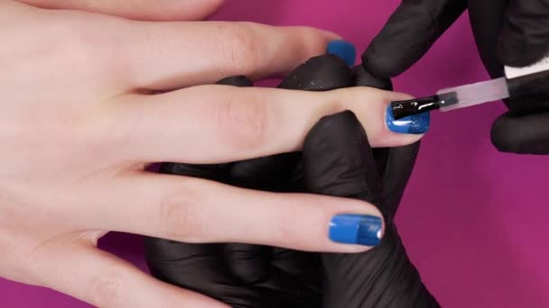 Маникюрша красит ногти клиентов с прозрачным лаком для ногтей на розовом фоне, макияж и ногти, закрыть нанесение лака для ногтей — стоковое видео