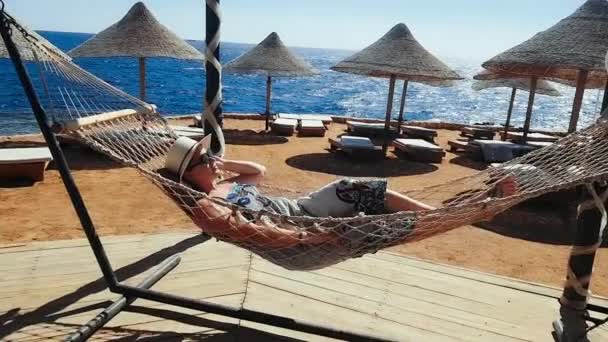 Vrouw rillingen in de hangmat op het strand, vakantie aan de zee, ontspannen op het strand, de zee en de recreatie, zand en blauw water — Stockvideo