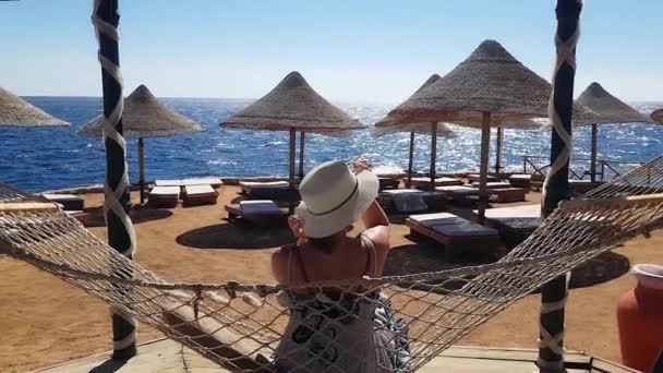 Femeia se răcește în hamac pe plajă, vacanță pe mare, relaxare pe plajă, mare și recreere, nisip și apă albastră — Videoclip de stoc