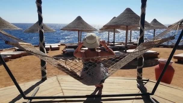 Vrouw rillingen in de hangmat op het strand, vakantie aan de zee, ontspannen op het strand, de zee en de recreatie, zand en blauw water — Stockvideo