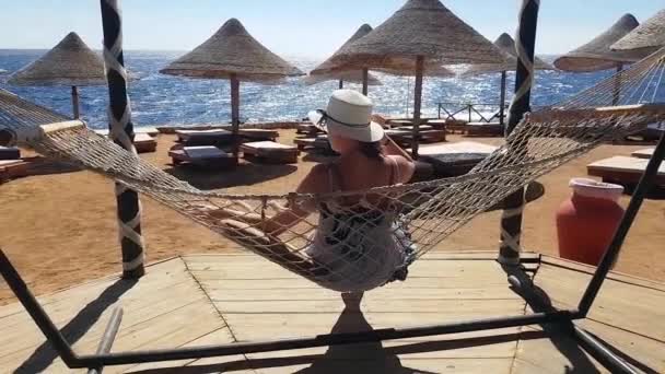 Vrouw rillingen in de hangmat op het strand, vakantie aan de zee, ontspannen op het strand, de zee en de recreatie, zand en blauw water — Stockvideo