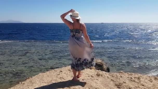 Mujer de pie en la colina en el lado del mar en un día soleado y ventoso con la celebración de su sombrero contra el viento, vacaciones en el mar, recuerdos de verano, relajarse en la playa, el mar y la recreación, arena y agua azul — Vídeos de Stock