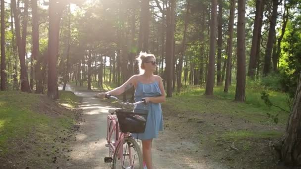 Ganska Europeiska kvinna i sundress promenader och rullar cykel i skogen på solnedgången, gå på den friska luften, cykeltur i sommar skog, Full Hd — Stockvideo