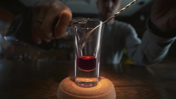 Ο μπάρμαν ρίχνει διαφανές αλκοόλ στην επίπεδη βολή με κόκκινο λικέρ με κουτάλι σε αργή κίνηση, χύνοντας αλκοόλ σε ένα μπαρ, μπάρμαν στη δουλειά, 4K UHD 60p ProRes HQ 422 — Αρχείο Βίντεο