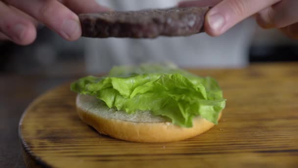 Chef cocina hamburguesa y pone chuleta a las hojas de ensalada verde fresca, restaurante de comida rápida, 4k UHD 60p HQ Prores 422 — Vídeo de stock