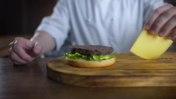 Chef adiciona queijo cheddar fatiado ao hambúrguer e coloca sobre a costeleta, cozinhando hambúrgueres em câmera lenta, restaurante de fast food, 4k UHD 60p Prores HQ 422 — Vídeo de Stock