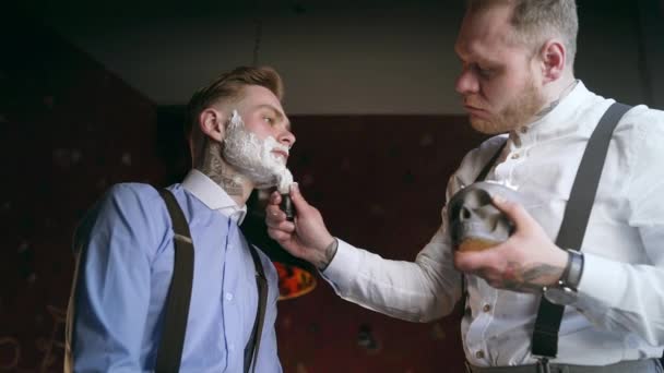 Tattooed barber applies foam by shaving brush on face of his tattooed client, barber shop in 30s mafia style, shaving salon, 4k UHD 60p Prores HQ 422 — Stock Video