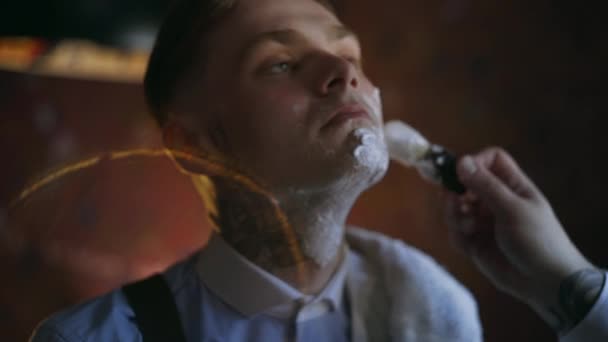Peluquero tatuado aplica espuma por cepillo de afeitar en la cara de su cliente tatuado, peluquería en el estilo de la mafia 30s, salón de afeitar, 4k UHD 60p Prores HQ 422 — Vídeo de stock