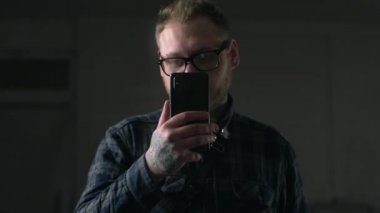 Gözlük adam dikkatlice karanlık ortamda telefonuna bakıyor, Gadget 'lar ile insanlar, internet sörf, sosyal ağlar bakarak, Mobila telefonda sohbet, Full HD ProRes 422 HQ