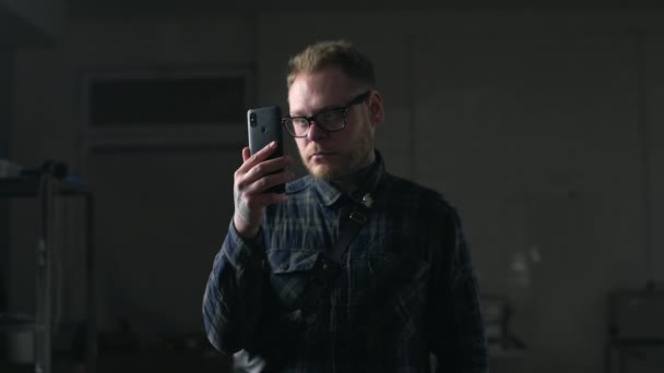 Man in glasses watches video on his smartphone in the dark environment, people with gadgets, surfing the internet, looking through the social networks, chat in the mobila phone, Full HD Prores 422 HQ — Stock Video