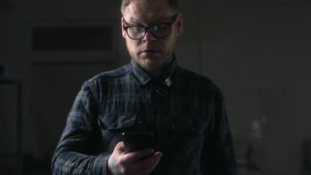 Człowiek w okularach patrzy uważnie na jego telefon w ciemnym otoczeniu, ludzie z gadżety, surfowanie po Internecie, patrząc przez sieci społeczne, czat w telefonie Mobila, Full HD ProRes 422 HQ — Wideo stockowe