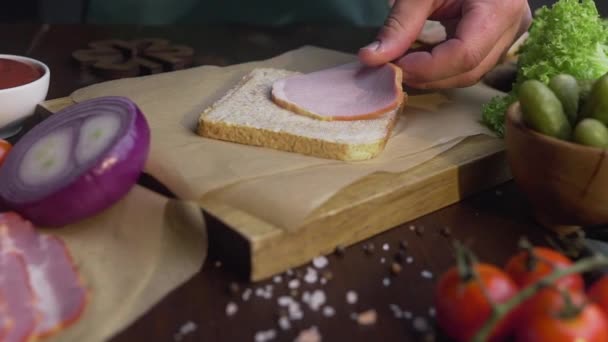 Primo piano video di fare il panino con prosciutto affettato e verdure, chef aggiunge prosciutto affumicato al panino, rendendo il fastfood a casa, cottura della carne, in cucina, Full HD Prores HQ 422 — Video Stock