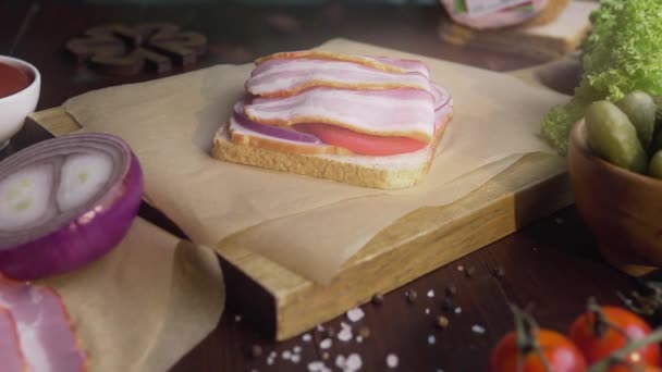 Göra smörgås med skivad bacon, Pickle och grönsaker på trä ombord i ljusstrålen, vilket gör Fastfood hemma, kött matlagning, i köket, full HD ProRes HQ 422 — Stockvideo