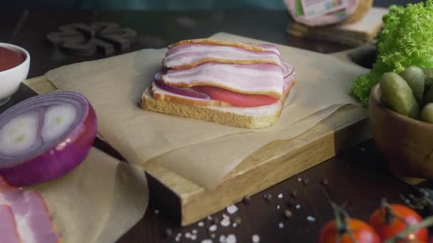 Het maken van de sandwich met gesneden spek, augurk en groenten op het houten bord in de lichtstraal, het maken van de fastfood thuis, vlees koken, in de keuken, Full HD ProRes HQ 422 — Stockvideo