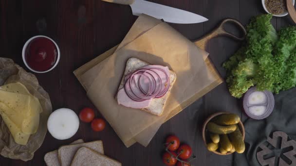 Pose plate de chefs à la main ajoute des tomates lissées au sandwich avec du jambon et des légumes tranchés sur la planche de bois dans le faisceau de lumière,, fabrication de la nourriture rapide à la cuisine, Full HD Prores HQ 422 — Video