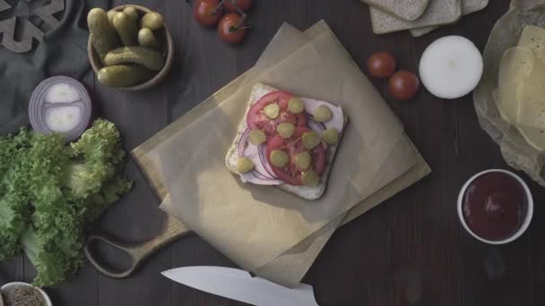 Letak roti lapis yang datar dengan ham dan sayuran di papan kayu dalam berkas cahaya, membuat makanan cepat saji di rumah, memasak daging, di dapur, Full HD Prores HQ 422 — Stok Video