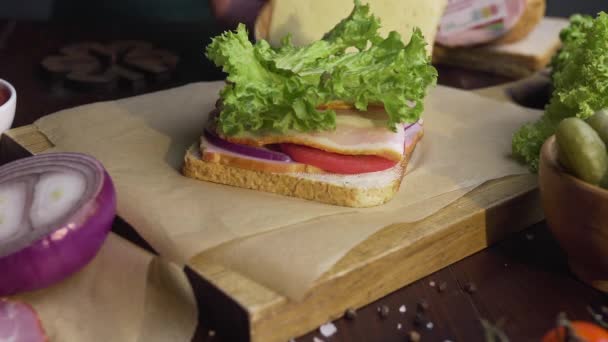 シェフは、光のビームで木製のボード上のハムとサラダでサンドイッチをファイナライズし、シェフの手は、キッチンでファーストフードを作り、サンドイッチを完成させ、フルHD Prores Hq 422 — ストック動画