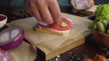 Aşçı, ışık demeti ahşap tahta üzerinde jambon ve sebze ile sandviç dilimlenmiş turşu ekler, evde fastfood yapma, et pişirme, mutfakta, Full Hd Prores Hq 422