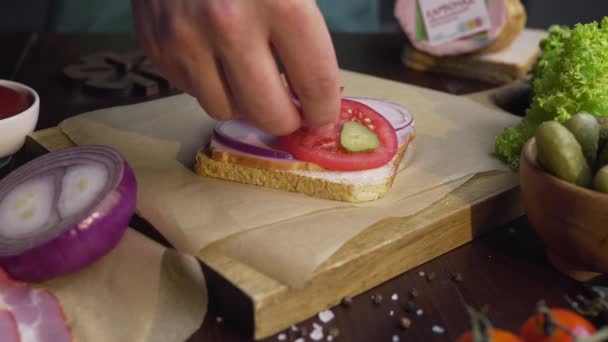 Le cuisinier ajoute des cornichons tranchés au sandwich avec du jambon et des légumes sur la planche en bois dans le faisceau de lumière, ce qui rend la nourriture rapide à la maison, cuisson de la viande, à la cuisine, Full HD Prores HQ 422 — Video