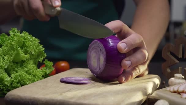 Chef corta la cebolla roja por el cuchillo afilado en el tablero de madera en la cocina, de cerca el video de cocinar la ensalada de verduras, rebanando las verduras, Full HD Prores 422 HQ — Vídeo de stock