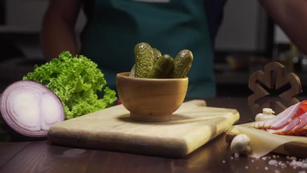 Diapositiva de zoom tiro: chef toma pepinillo del tazón en la mesa de la cocina, verduras enlatadas, ingredientes para cocinar, pepinos enlatados, Full HD Prores 422 HQ — Vídeo de stock