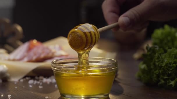Chef dips houten honing stok aan de glazen kom met vloeibare honing, koken met honing, zoete maaltijden met natuurlijke ingrediënten, gezonde voeding, Full HD ProRes 422 HQ — Stockvideo