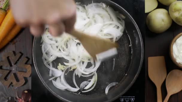 Vidéo de pose à plat : le chef agite l'oignon haché par une spatule de cuisine en bois sur la casserole chaude, dessus de table de cuisine végétarienne, oignons frits, légumes blancs, Full HD Prore 422 HQ — Video