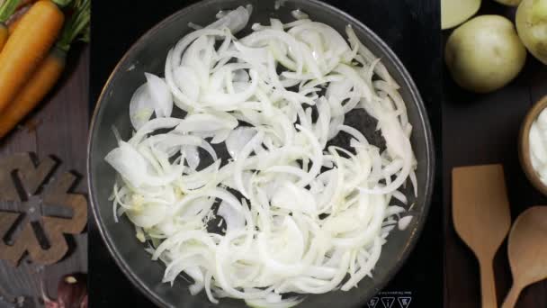 Vidéo de pose à plat : le chef ajoute de l'huile d'olive à la poêle chaude et brasse l'oignon haché par une spatule de cuisine en bois, une table de cuisson végétarienne, des oignons frits, des légumes blancs, Full HD Prore 422 HQ — Video
