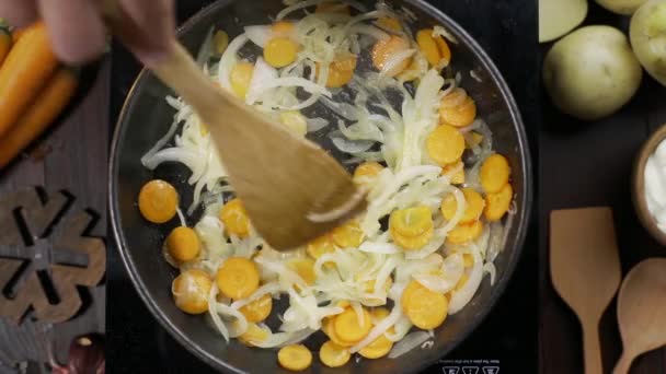 Flat lay video: шеф-повар перемешивает нарезанную морковку и лук на горячей сковороде деревянным кухонным лопатком, столешницей рагу, жареным луком и морковью, овощами бланш, Full HD Prores 422 HQ — стоковое видео