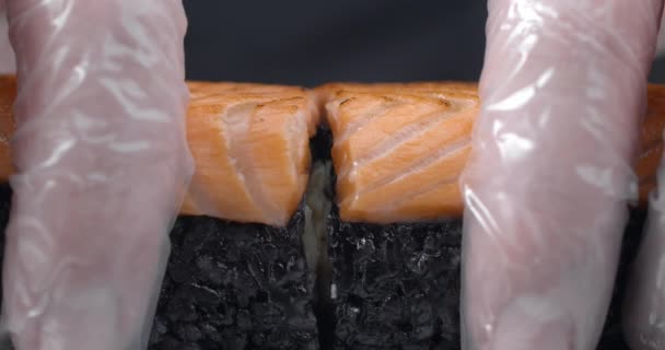 Chef splitst in een halve Sushi broodje met zwarte rijst en zalm, het koken van de rauwe rode vis, knapperige zalm sushi roll, Aziatische keuken, 4k DCI 60p Slow Motion ProRes HQ 10 bit — Stockvideo