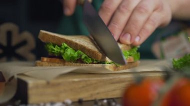 Man cuts club sandwich in a half by sharp knife on a wooden board at the kitchen, making of the fastfood at home, chef is cooking sandwich, 4k UHD Prores HQ 422