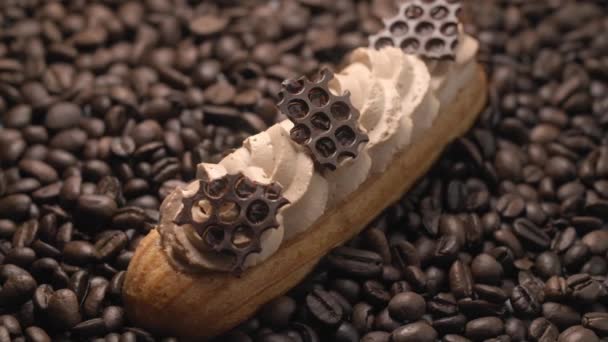 Eclair con crema di caffè e pezzi di cioccolato si trova sui chicchi di caffè nel fascio di luce, dessert in caffè, ripieno per eclairs, pasticceria choux, Full HD 120fps Prores 422 HQ 10 bit — Video Stock