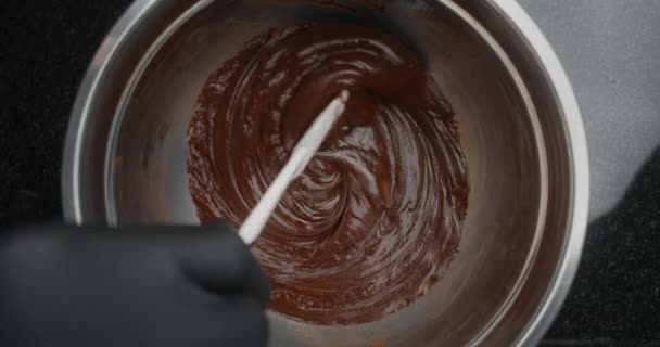 Tabletop shot: Chef rührt langsam geschmolzene Schokolade in Metallschüssel bei schwacher Hitze in Zeitlupe, Rohstoffe für die Herstellung von Süßigkeiten und Schokolade, Kochen der süßen Desserts, Herstellung von Schokoladenbonbons, 4k — Stockvideo