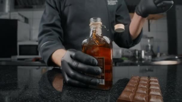 Zoom: chef in grembiule nero e guanti apre la bottiglia di cognac e bung vola via al rallentatore, aprendo la bottiglia di bevanda alcolica, spruzzi di whisky, video cibo da tavolo, Full HD 240 — Video Stock