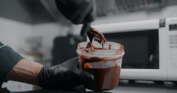 Кондитер медленно перемешивает расплавленный шоколад в пластиковой банке, сырье для изготовления сладостей и шоколада, приготовление сладких десертов, изготовление шоколадных конфет, 4k 120p Прорес HQ 10 бит — стоковое видео